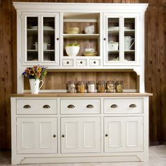 a white cabinet with glass doors and drawers in a room that has wood paneling on the walls