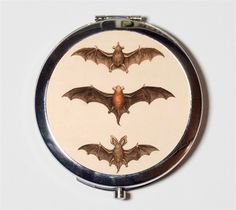 three bats on a white background are depicted in this compact mirror, which is decorated with silver trim