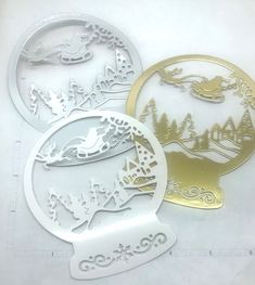 three paper cutouts with christmas scenes and trees in the background, one is gold