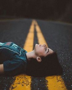 a young boy laying on the side of an empty road with his head up and eyes closed