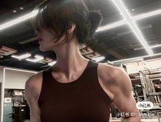 a woman standing in a gym with her arms crossed and looking to the side while wearing a brown tank top