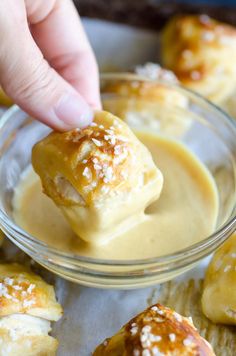 a person dipping some kind of food into a glass bowl with sauce in it and other pastries on the side