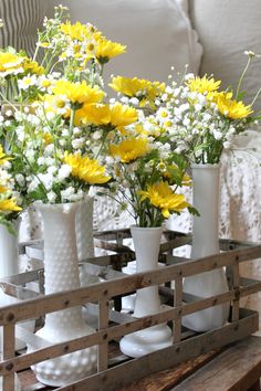 vases filled with yellow and white flowers sit on a wooden table in front of a couch