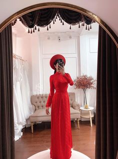 a woman in a red dress and hat taking a selfie with her cell phone