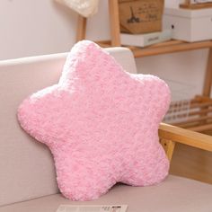 a pink star shaped pillow sitting on top of a white couch next to a wooden chair