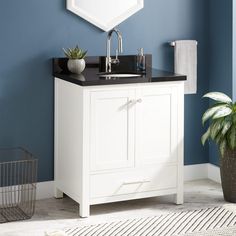 a white bathroom vanity with black counter top and mirror above it, next to a potted plant