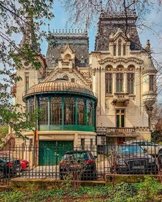 an old house with cars parked in front of it and a fence around the yard