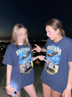 two young women standing next to each other in front of a city skyline at night