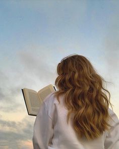 a woman with long red hair is looking at the sky while holding an open book