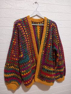 a colorful crocheted sweater hanging on a white brick wall