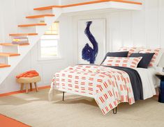 an orange and white bed in a bedroom next to a stair case with books on it