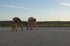 two horses standing on their hind legs in the middle of an empty road at sunset