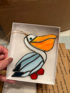 a hand holding up a stained glass bird in front of a cardboard box with string