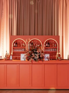 an orange bar with lots of bottles and flowers on the top shelf next to it