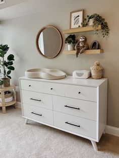 a white dresser sitting next to a mirror and potted plant