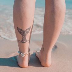 a woman's legs with tattoos on them standing in the sand at the beach