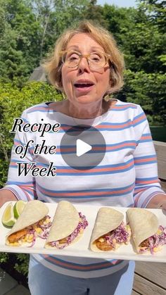 a woman holding a plate with three burritos on it and the words recipe of the week written in front of her