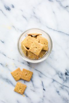 a glass bowl filled with crackers sitting on top of a marble counter next to two small pieces of food