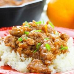 a red plate topped with rice and meat covered in sauce next to an orange slice