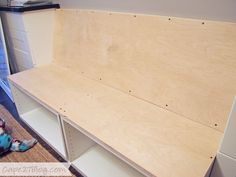 an unfinished shelf is sitting on the floor in front of a wall with shelves and cupboards