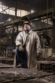 an older man in a white coat and safety glasses is sitting on a piece of wood