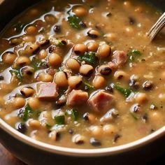 a bowl of soup with beans, ham and spinach in it on a wooden table