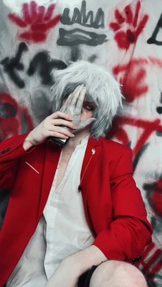 a man with white hair and red jacket sitting in front of a wall covered in graffiti