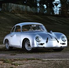 an old silver sports car parked in front of a hill