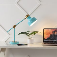 an open laptop computer sitting on top of a white desk next to a potted plant