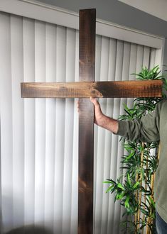 a man holding a wooden cross in front of a window with vertical blinds on it