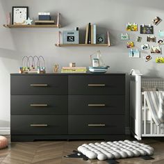 a baby's room with a dresser, crib and bookshelf on the wall