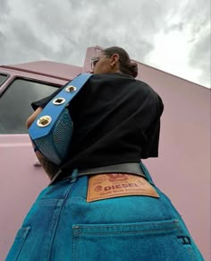 a woman with a blue purse on her back standing in front of a pink truck