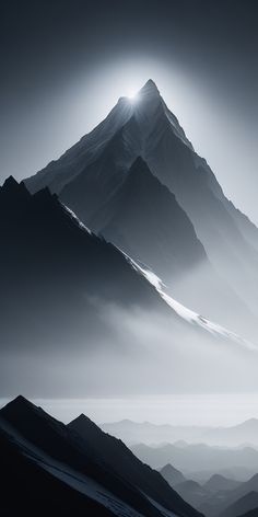 black and white photograph of mountains with sun shining through the foggy clouds in the distance