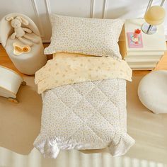 a small child's bed with yellow and white comforter, pillows and stuffed animals