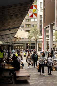 many people are walking around in an open area with tables and benches on either side of the walkway