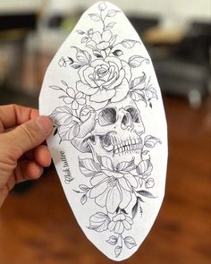 a person holding up a piece of paper with a skull and flowers on it