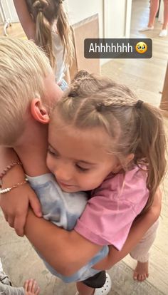 two children are hugging each other in the middle of a room with people looking on