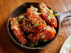 a skillet filled with chicken wings covered in sesame seeds and garnished with scallions