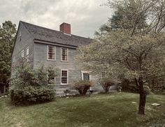 an old gray house sitting on top of a lush green field next to a tree