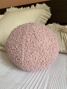 a pink ball sitting on top of a bed next to pillows and throw pillows with ruffled edges