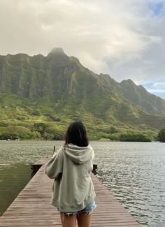 a woman is standing on a dock looking at the water and mountains in the distance