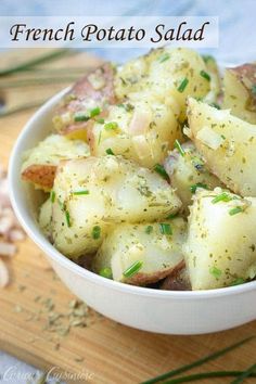 a white bowl filled with potatoes on top of a wooden cutting board next to garlic