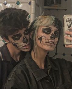 two people with painted faces taking a selfie in a mirror together, one person is holding a cell phone