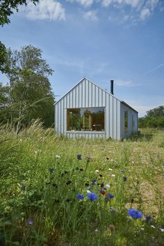 a small metal building sitting in the middle of a lush green field with wildflowers