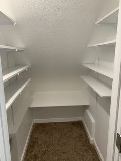 an empty walk in closet with white shelving and carpeted flooring is shown