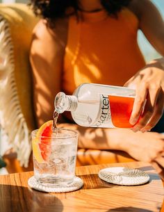 a woman pouring a drink into a glass on top of a wooden table