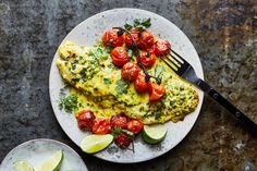 an omelet with tomatoes and limes on a plate next to a fork