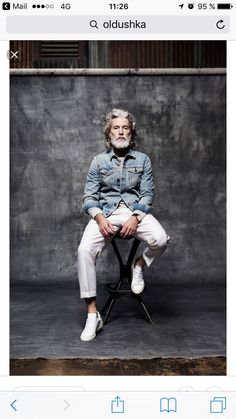 a man sitting on top of a chair in front of a cement wall and wearing white pants