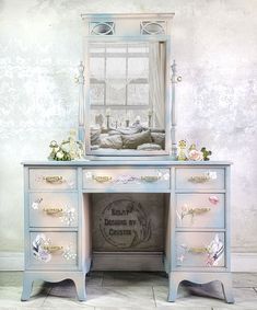 an old dresser with flowers and a mirror on it's top, in front of a white wall