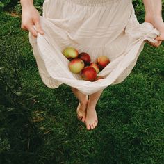 a woman is standing in the grass with apples in her hands and wearing a white dress